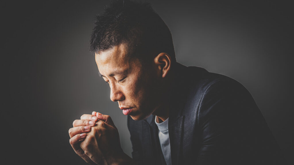 Chinese Christian man with his eyes closed and hands clasped in prayer.