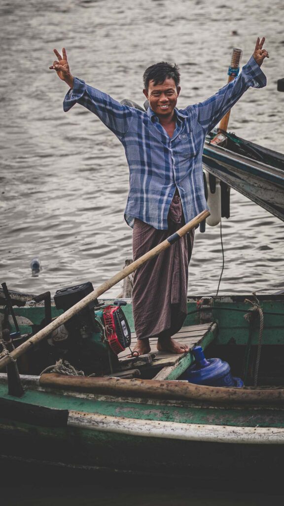 Burmese fisherman standing in a traditional wooden boat in Myanmar.