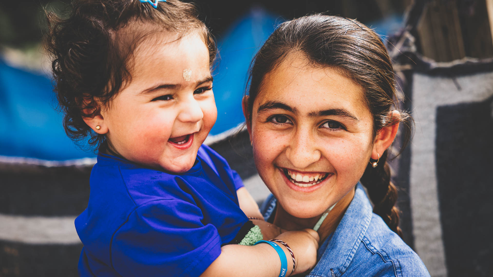 Two young girls smiling together outdoors in Iraq.