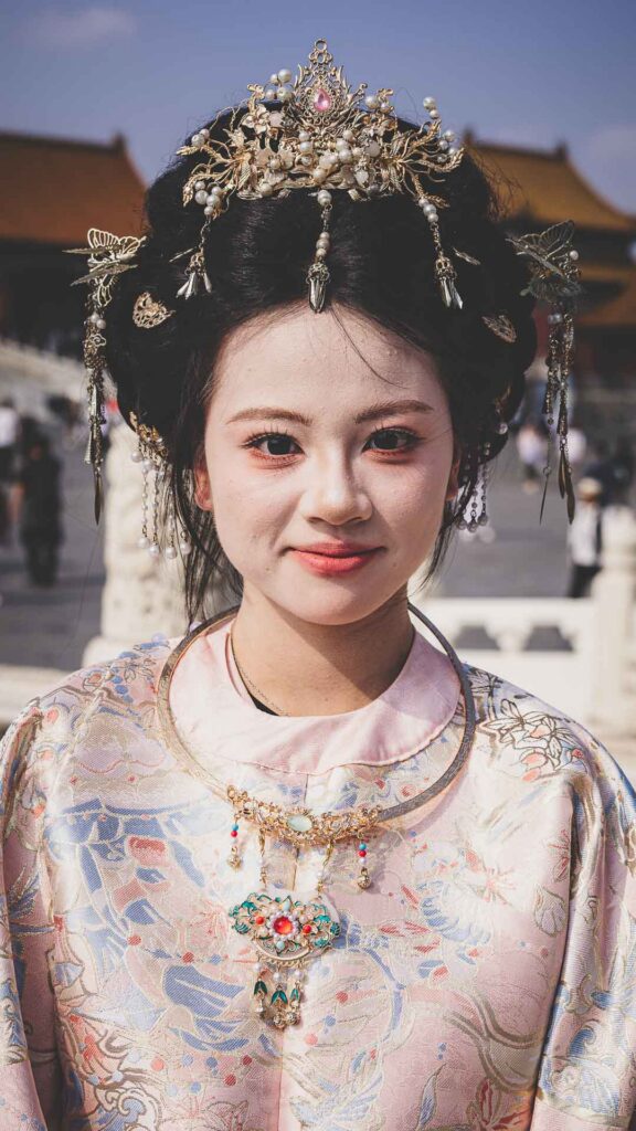Portrait of a young woman wearing ornate traditional-style Chinese dress and headdress at the Forbidden City in Beijing.