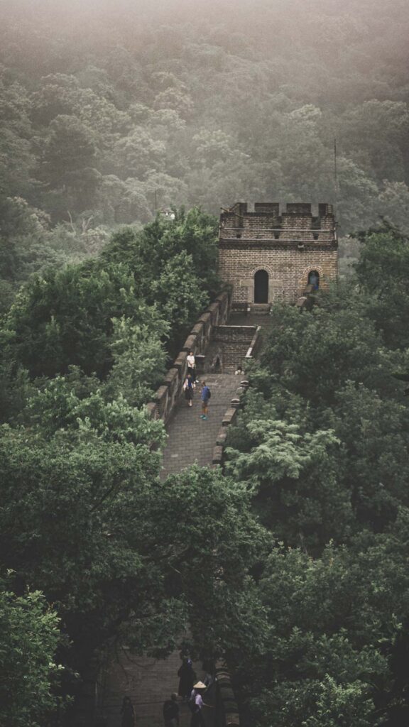 Great Wall of China winding through forested mountains toward a historic watchtower.
