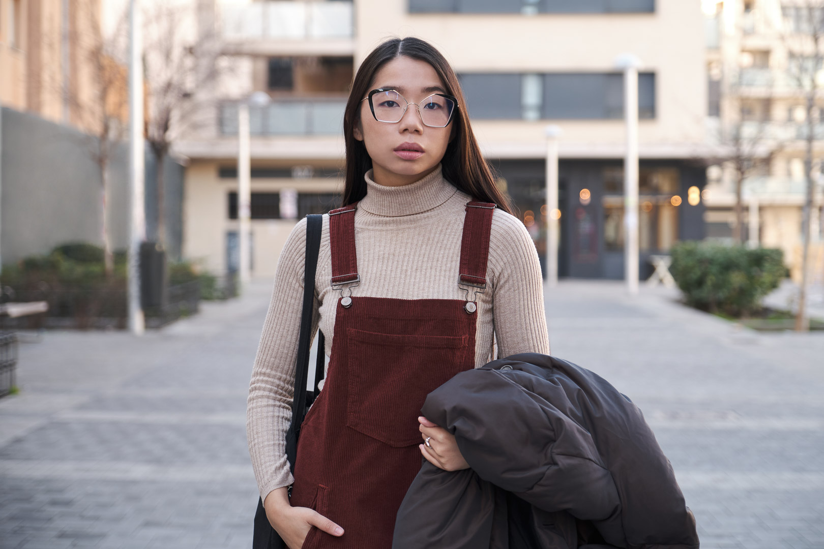 Young Asian woman wearing glasses standing in an urban setting.