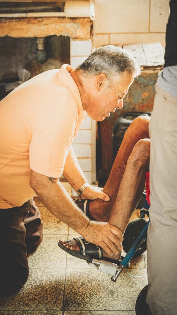 Cuban pastor kneeling beside a man in a wheelchair and praying for him.