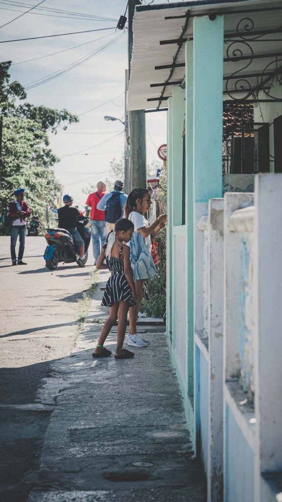 People gathered along a residential street beside colorful homes in Cuba.