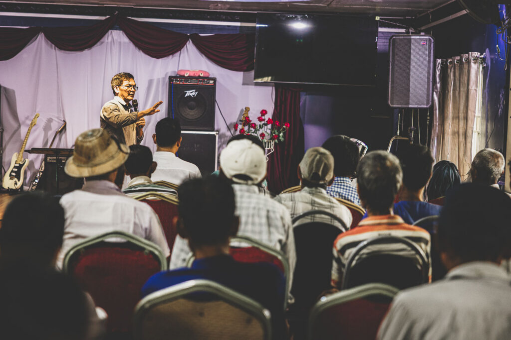 Local pastor speaking to people gathered for a church outreach event in Myanmar.