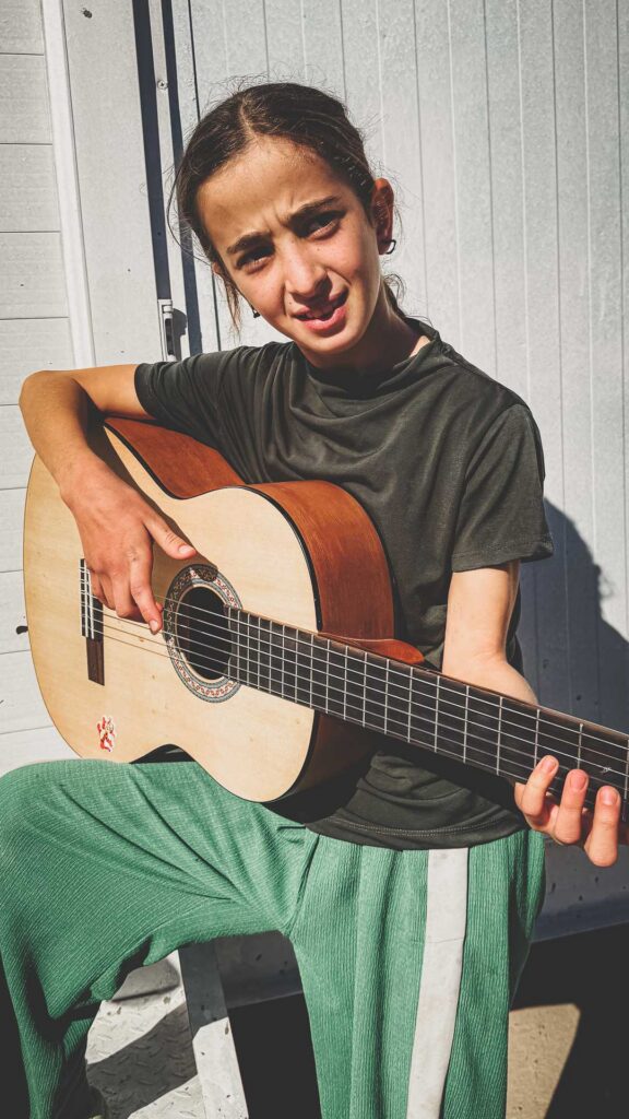 Young refugee student learning guitar during a music class in Iraq.