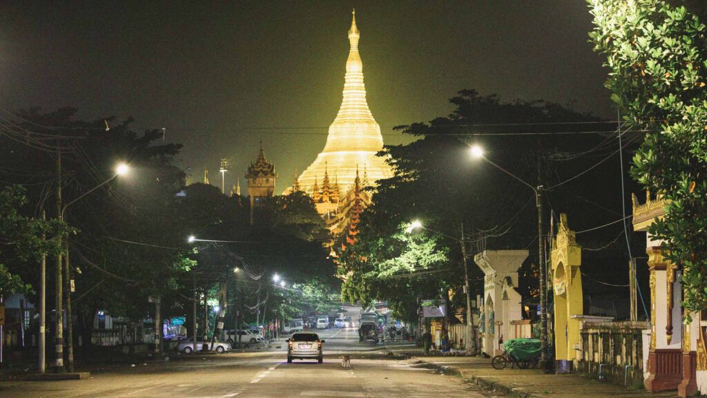 Shwedagon Pagoda illuminated above a street in Yangon, Myanmar, at night.