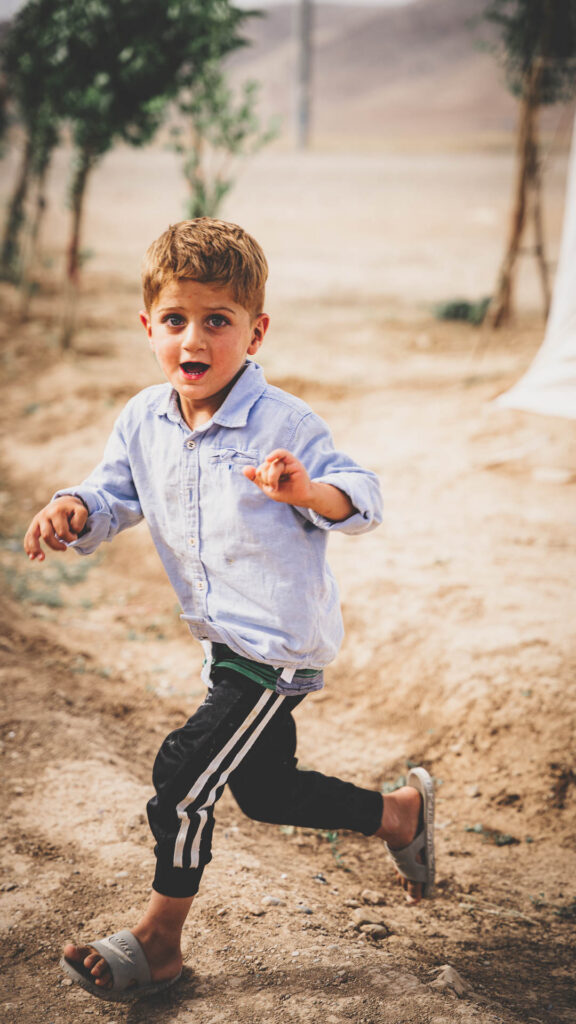 Young boy running along a dusty road in Iraq.