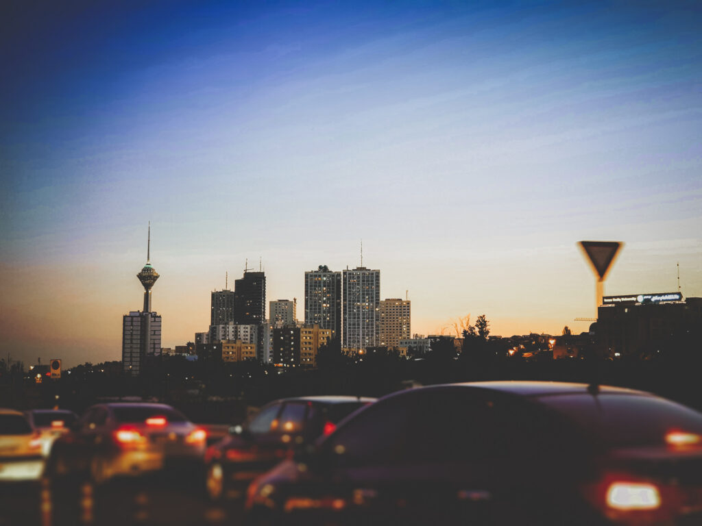 Traffic moves past a city skyline at sunset in Iran.
