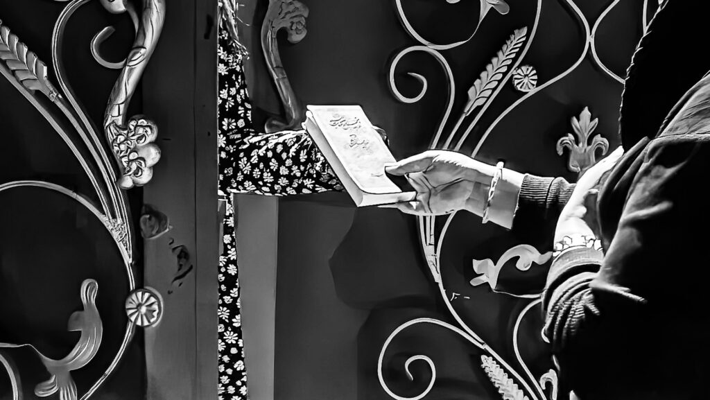 Person holding and reading a book beside an ornate metal doorway.