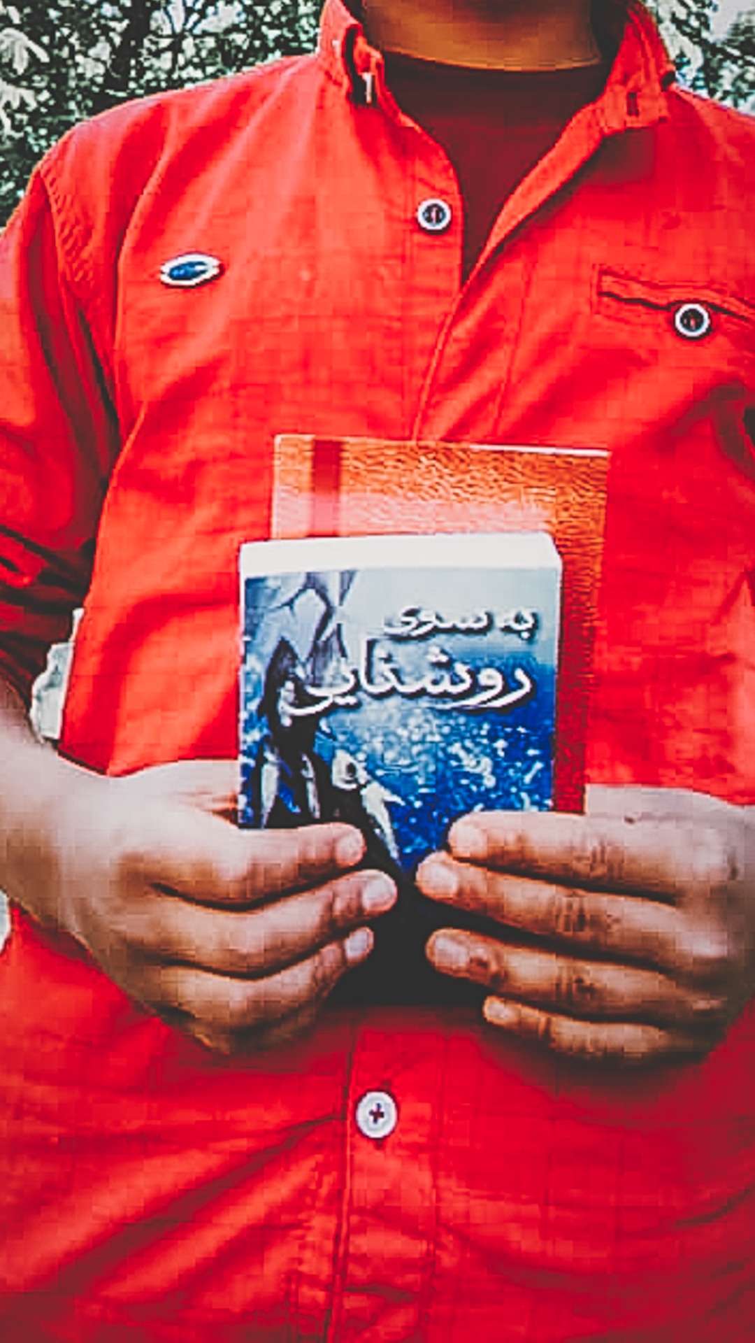 Person holding a Persian-language book in front of a red jacket.