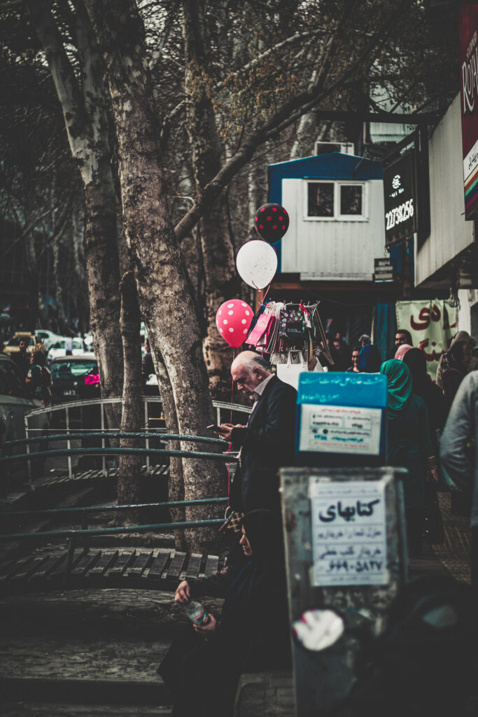 People walking along a tree-lined urban street in Iran.