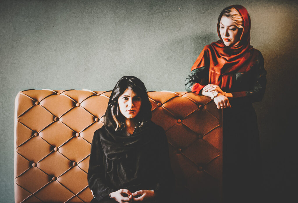 Two women in an indoor setting, with one seated and the other standing behind a sofa.