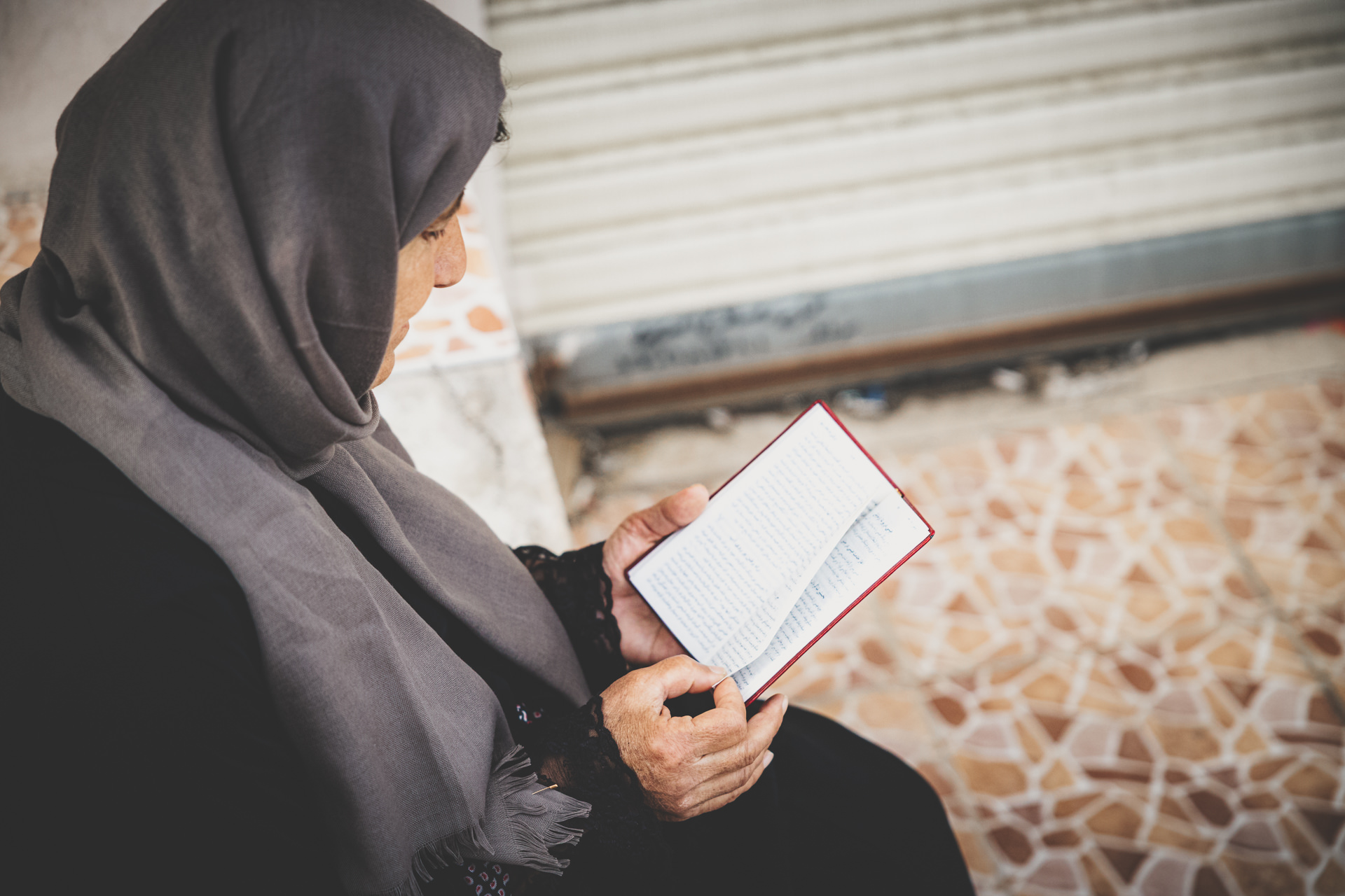 Woman in a headscarf reading a book while seated.